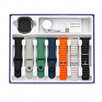 A boxed set of smartwatch bands displayed in a white tray with a blue outer border. The set includes a smartwatch with a black screen, a white charging cable, a user manual, and multiple interchangeable bands in black, light gray, green, navy, orange, white, and dark gray.